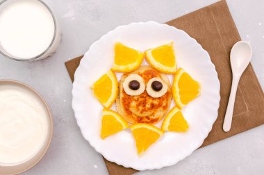 Krepten komik güneş yüzlü atıştırmalık, tabakta turuncu. Tatlı çocuklar bebeğin tatlı tatlısını, sağlıklı kahvaltısını, öğle yemeğini, sütlü ve ekşi kremalı yemek sanatını gri beton arka planda, üst manzarada.