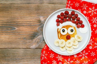 Noel Baba 'nın yüzü tatlı taze ahudududulu krep tabakta muz, tahta zeminde Noel çorabı çocuklar için kahvaltı. Xmas yemek tatlısı, yeni yıl süslemeleri..