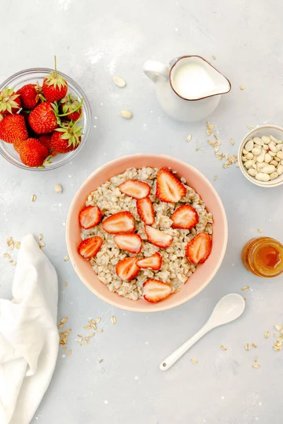 Oatmeal porridge with summer strawberries berries. Porridge oats in bowl with honey,milk,nuts. Healthy food breakfast,lifestyle,dieting, proper nutrition. Top view flat lay on gray table background.