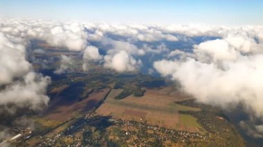 Uçaktan hava perspektifi, uzak şehrin yüksek irtifasındaki uçak penceresi, güneşli bir günde gökyüzünde uçan beyaz kabarık kümülüs bulutları. Doğa, hava, manzara..