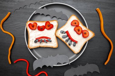 Cadılar bayramında kızarmış ekmek, tereyağı, çilek, şeker, servis tahtası, siyah arka planda yarasalar. Çocuklar tatlı tatlı tatlı kahvaltı öğle yemeği.