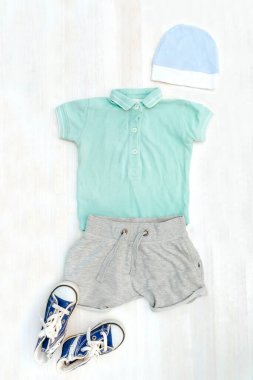 Şirin bir bebek tulumu, şort, şapka, spor ayakkabı. Çocuklar, çocuk kıyafetleri, elbiseler ve pastel mavisi aksesuarlar. Yenidoğan, çocuk modası, erkek kıyafeti. Düz yatış, üst görünüm, model.
