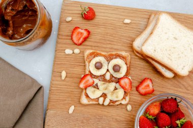 Komik baykuş suratlı tost ekmeği, fıstık ezmesi, muz, ahşap tahtada çilek. Tatlı çocuklar bebeğin tatlı tatlısını, sağlıklı kahvaltısını, öğle yemeğini, gri arka planda yemek sanatını, üst manzarayı....