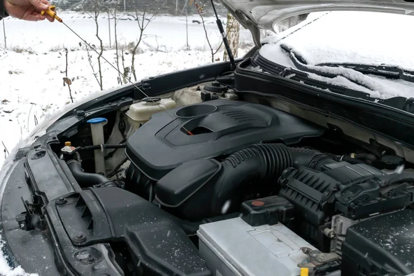 Close-up side view of auto mechanic man checking engine oil level in car, workshop, garage. car repairing service with open hood,outside backyard in winter.