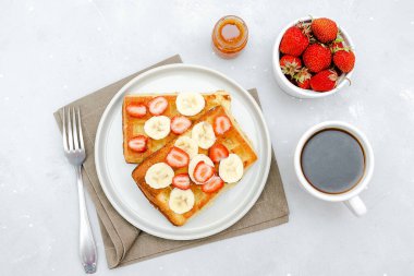 Çilekli Belçika waffleları, muzlar, konsantre süt, tabakta bal, bir fincan kahve espresso. Lezzetli kahvaltı, tatlı tatlı yiyecekler. Seçici odak, üst manzara düzlüğü..