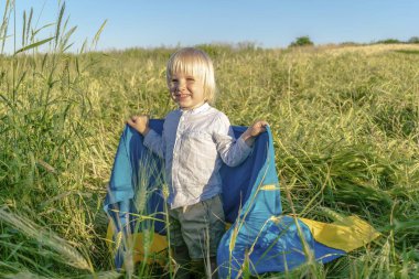 Elinde buğday tarlasında Ukrayna ulusal mavi bayrağı taşıyan şirin çocuk çocuğu. Savaş, Rusya ile Ukrayna arasında askeri işgal. Bağımsızlık, Bayrak, Anayasa, Kiev Günü.