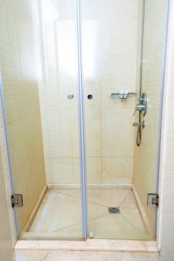 Büyük, modern, lüks otel banyosunun iç tasarımı bej kaplamalı duş kabini, paslanmaz yağmur başlığı, el yapımı duş, şeffaf cam kapı, duş şişeleri, şampuan jeli..