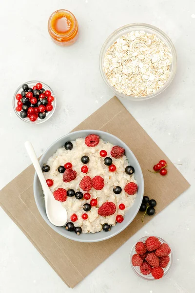 Oatmeal porridge with summer raspberry, currant berries,honey. Porridge oats in bowl with fruits. Healthy food breakfast,lifestyle,dieting, proper nutrition.Top view flat lay on gray table background.