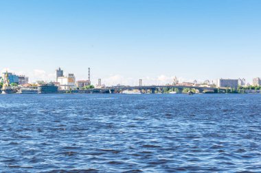 Scenic nature travel cityscape river Dnipro with blue water and metal pedestrian bridge at sunny summer day in Kiev. View from inside river, ship on water-Kiev Ukraine,11 June 2021.