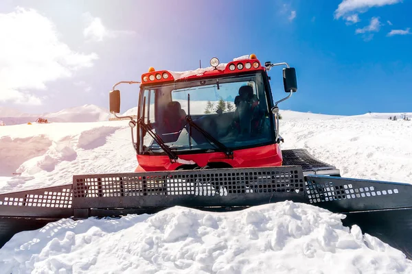 Red modern snowcat ratrack with snowplow,snow grooming machine,remover truck preparing ski slope,piste,hill at alpine skiing winter resort. Heavy machinery,tractor mountain equipment track vehicle.