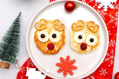 Christmas deers face shaped pancake with sweet fresh raspberry berry and cheese on plate for kids baby children breakfast dinner. xmas food with new year decorations on gray background close up.