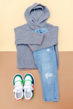 Spor ayakkabılı kazak ve kot pantolon. Bahar, sonbahar ya da yaz için bej rengi kahverengi arka planda bebek kıyafetleri ve aksesuarlar. Moda çocuk kıyafeti. Düz yatıyordu, üstten, yukarıdan..