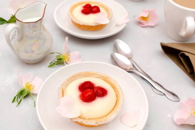 Lezzetli kırmızı ahududu çilekli kremalı tartlar, pastalar. Sütlü kahve tabağında gurme şekerli tatlı. Gri masada olgun böğürtlenli tatlı pastalı peynirli kek..