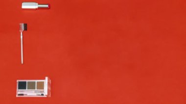 New year beauty cosmetics stop motion animation with appearing brushes,lipstick,eyeshadow,powder,accessories,balls decorations on red christmas background. Stylish fashion geometric Flat lay.