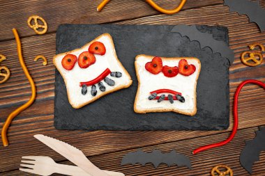 Cadılar bayramında kızarmış ekmek, tereyağı, çilek, şeker, servis tahtası, siyah arka planda yarasalar. Çocuklar tatlı tatlı tatlı kahvaltı öğle yemeği.