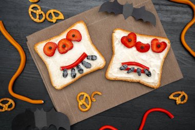 Cadılar bayramında kızarmış ekmek, tereyağı, çilek, şeker, servis tahtası, siyah arka planda yarasalar. Çocuklar tatlı tatlı tatlı kahvaltı öğle yemeği.