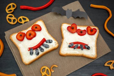 Cadılar bayramında kızarmış ekmek, tereyağı, çilek, şeker, servis tahtası, siyah arka planda yarasalar. Çocuklar tatlı tatlı tatlı kahvaltı öğle yemeği.