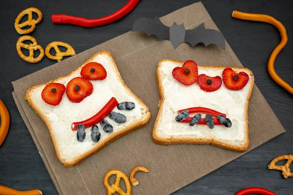 Cadılar bayramında kızarmış ekmek, tereyağı, çilek, şeker, servis tahtası, siyah arka planda yarasalar. Çocuklar tatlı tatlı tatlı kahvaltı öğle yemeği.