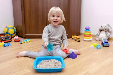 Sevimli küçük çocuk evde kinetik kumla duyusal kutuda oynuyor. Güzel motor beceriler geliştiriyor. Erken duyusal eğitim. Etkinlikler Montessori.art yaratıcılık, kreşte zanaat, anaokulu.