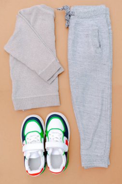 Bebek ayakkabısı, tişört, kazak ve kot pantolon. Bahar, sonbahar ya da yaz için çocuk kıyafetleri ve aksesuarlar. Moda çocuk kıyafetleri, bej rengi kahverengi arka plan..