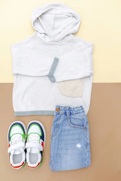 Jumper and jeans pants with sneakers. Set of baby children\'s clothes and accessories for spring, autumn or summer on beige brown background. Fashion kids outfit. Flat lay, top view, overhead.