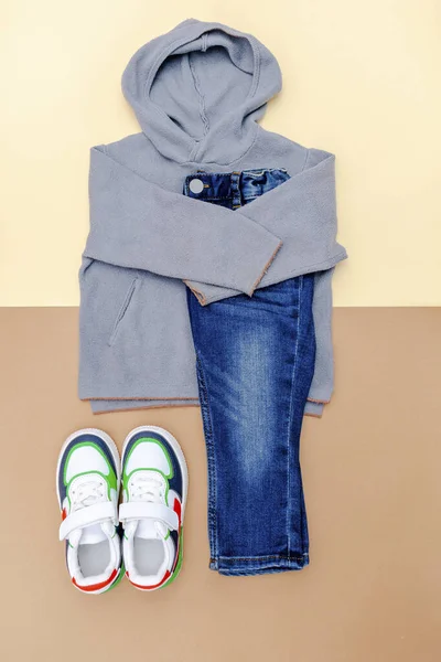 Jumper and jeans pants with sneakers. Set of baby children\'s clothes and accessories for spring, autumn or summer on beige brown background. Fashion kids outfit. Flat lay, top view, overhead.