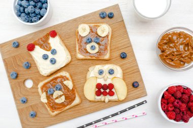 Komik şirin ayı, maymun, tilki, baykuş suratlı sandviç fıstık ezmeli tost ekmeği, muz, yabanmersini, ahududu, süt. Çocuklar bebeğin tatlı, sağlıklı kahvaltı, öğle yemeği sanatı, yakın plan, üst manzara..