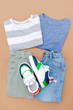 Bebek ayakkabısı, gömlek ve kot pantolon. Bahar, sonbahar ya da yaz için çocuk kıyafetleri ve aksesuarlar. Moda çocuk kıyafetleri, bej kahverengi arka planda giysiler. Düz yatıyordu, üstten, yukarıdan..