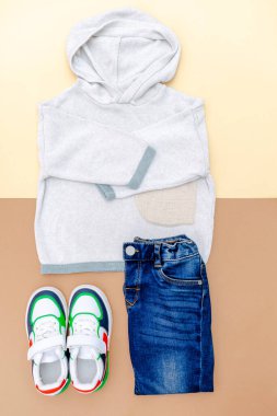 Spor ayakkabılı kazak ve kot pantolon. Bahar, sonbahar ya da yaz için bej rengi kahverengi arka planda bebek kıyafetleri ve aksesuarlar. Moda çocuk kıyafeti. Düz yatıyordu, üstten, yukarıdan..