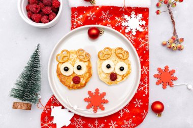 Christmas deers face shaped pancake with sweet fresh raspberry berry and cheese on plate for kids baby children breakfast dinner. xmas food with new year decorations on gray background close up.
