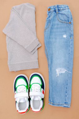 Bebek ayakkabısı, tişört, kazak ve kot pantolon. Bahar, sonbahar ya da yaz için çocuk kıyafetleri ve aksesuarlar. Moda çocuk kıyafetleri, bej rengi kahverengi arka plan..