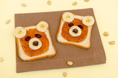 Funny cute bear faces sandwich toast bread with peanut butter, banana,nuts. Kids childrens baby's sweet dessert healthy breakfast lunch food art on plate,close up,top view.