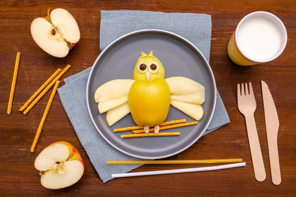 Funny owl face shape snack with apple, wheat crispy bread straw on plate,milk in glass. Cute kids childrens baby\'s sweet dessert, healthy breakfast,lunch, food art on wooden background,top view.