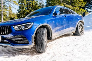 Lüks mavi sedan araba farları soğuk kış günü karda dışarıda park edilmiştir.Modern otomobil yatak havasında araç, macera ekstrem spor, Karpatlar dağları, Ukrayna, 15 Mart 2022.