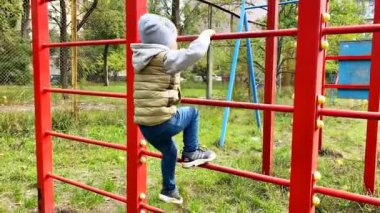 Arka manzara sevimli sevimli beyaz çocuk modern oyun bahçesinde merdivene tırmanıyor. Açık havada çocuklar için sokak sporları, fiziksel gelişim, çocukluk, anaokulu.