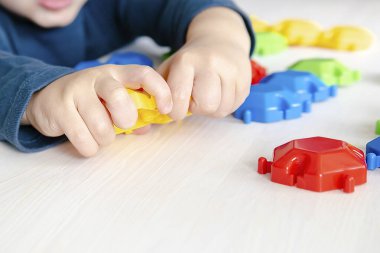 Mozaik yapımcısıyla oynayan küçük bir çocuk. Bebek, plastik blokların figürlerini yapıyor. Çocuk mantığı, motor becerileri gelişimi, anaokulu. Erken duyusal eğitim..