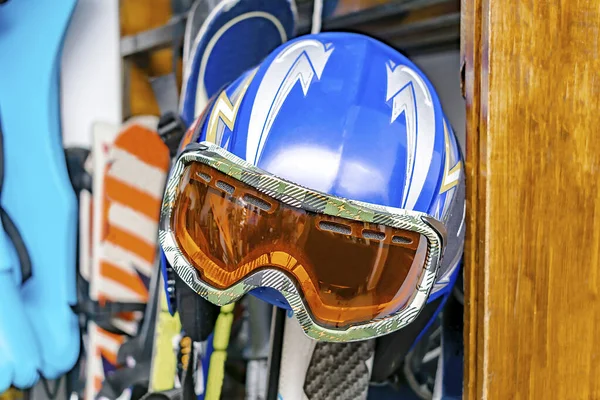 Helmet, ski mask, ski hanged on customized wooden wall mount at warehouse for seasonal storage at ski resort. Extreme winter sport equipment handling at home