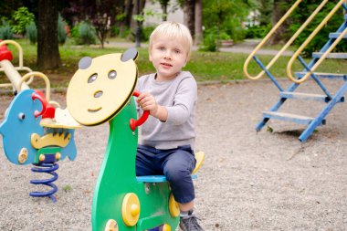 Şirin, komik, sarışın, küçük çocuk çocuk çocuk çocuk parkta salıncakta sallanıyor. Çocuklar fiziksel, duygusal gelişim ve çocukluk kreşi, anaokulu konsepti..