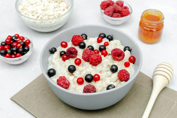 Oatmeal porridge with summer raspberry, currant berries,honey. Porridge oats in bowl with fruits. Healthy food breakfast,lifestyle,dieting, proper nutrition.Top view flat lay on gray table background.