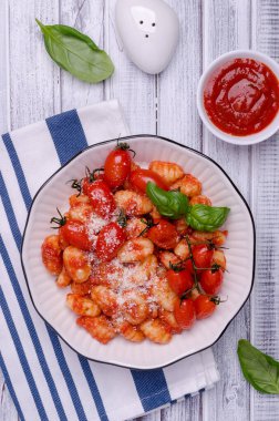 Domatesli gnocchi, kırmızı sos, peynir ve fesleğen yapraklı hafif ahşap zemin. Üst Manzara. Seçici odak.