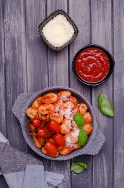 Gri ahşap arka planda domatesli gnocchi, kırmızı sos, peynir ve fesleğen yaprakları. Üst Manzara. Seçici odak.