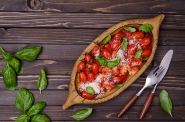 Kahverengi ahşap arka planda domatesli gnocchi, kırmızı sos, peynir ve fesleğen yaprakları. Üst Manzara. Seçici odak.