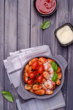 Gri ahşap arka planda domatesli gnocchi, kırmızı sos, peynir ve fesleğen yaprakları. Üst Manzara. Seçici odak.