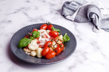 Domatesli gnocchi, kırmızı sos, mermer zemin üzerinde peynir ve fesleğen yaprakları. Seçici odaklanma. Üst görünüm. 