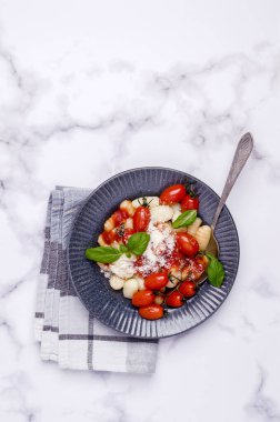 Domatesli gnocchi, kırmızı sos, mermer zemin üzerinde peynir ve fesleğen yaprakları. Seçici odaklanma. Üst görünüm. 