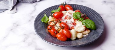 Domatesli gnocchi, kırmızı sos, mermer zemin üzerinde peynir ve fesleğen yaprakları. Seçici odaklanma. Üst görünüm. 