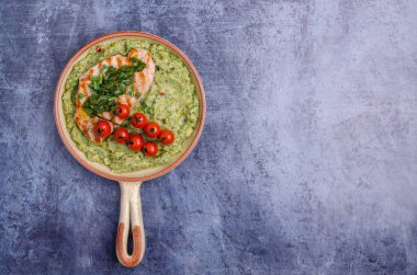 Mavi arka planda yeşil patates püresi ve domatesli ızgara biftek. Üst görünüm.