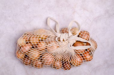 Hafif arka planda örgü bir çantada taze sarı soğan. Sıfır israf kavramı. Üst Manzara. Boşluğun bir kopyası.