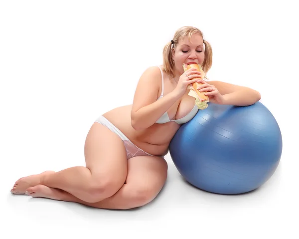 Divertente immagine di donna in sovrappeso seduta su una palla fitness mangiare panino grande . — Foto Stock