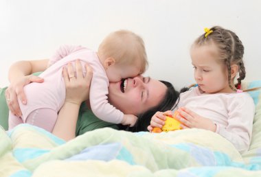 mutlu bir aile. çocuklarıyla birlikte yatağa oynayan genç anne.